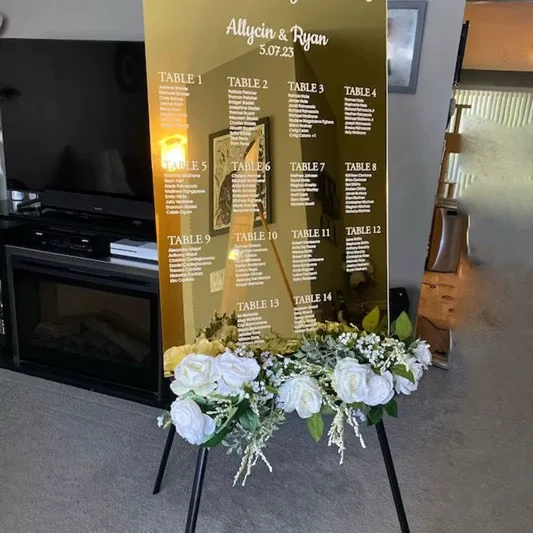 Seating chart dorado personalizado con arreglo de rosas blancas para una boda